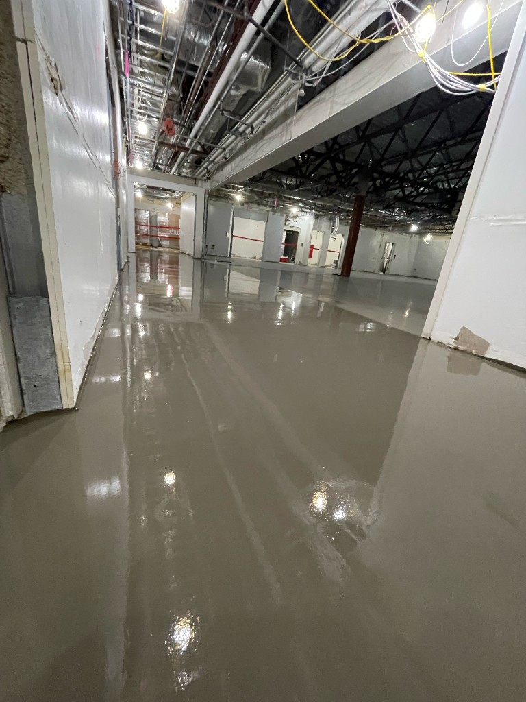 Freshly poured light grey floor coating in a corridor with exposed ceiling utilities