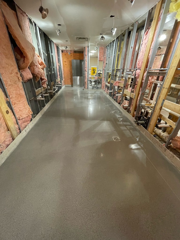 Hallway under construction with polished grey floor and exposed wall framing