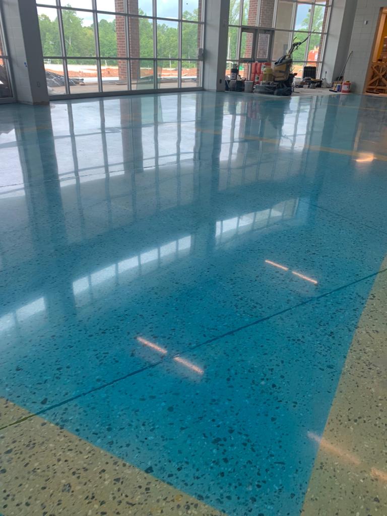 High-gloss teal terrazzo floor with aggregate in a large institutional corridor